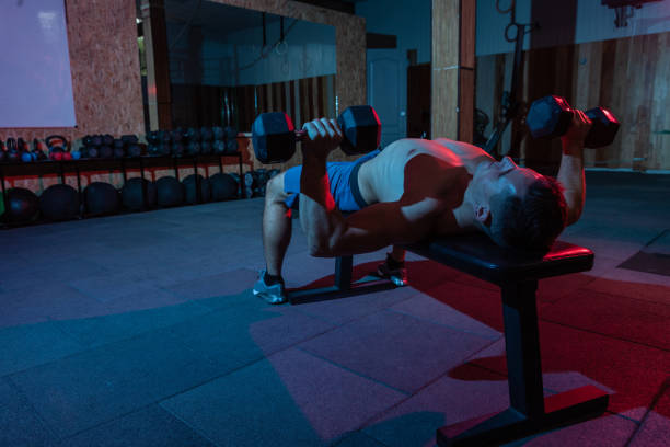 istock Muscular powerful man training bench press with dumbbells exercise in red blue neon light 1313692912