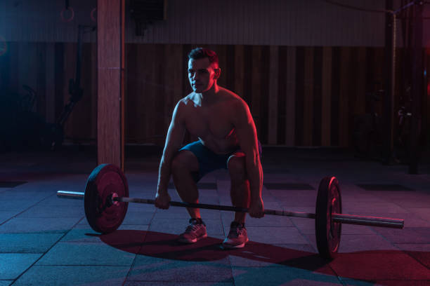 istock Working out by lifting weights in a cross-training gym. Muscular powerful man doing deadlift with a heavy barbell in red blue neon light 1313692982