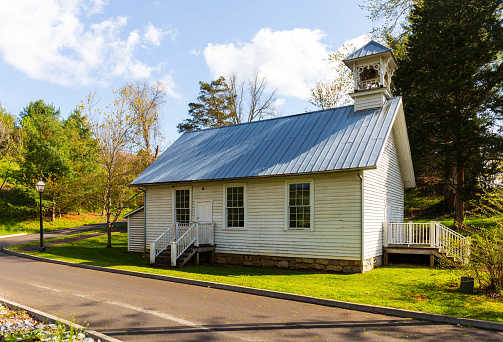 Jonesborough, TN, USA--9 April 2021: The 1866 Oak Hill School house sets behind the town Heritage Alliance. It served its community as a school and a community center intil the 1950s.  Blue sky with clouds, green grass, spring color.