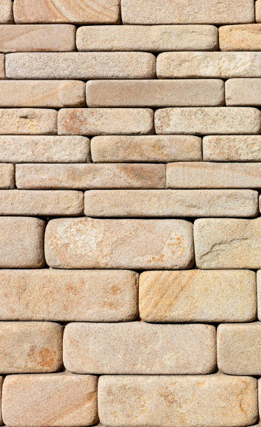 The wall is faced with hewn yellow sandstone of various thicknesses with rounded ribs. The background and texture of the wall is made of hewn sandstone with rounded edges. Vertical image, close-up. roughhewn stock pictures, royalty-free photos & images