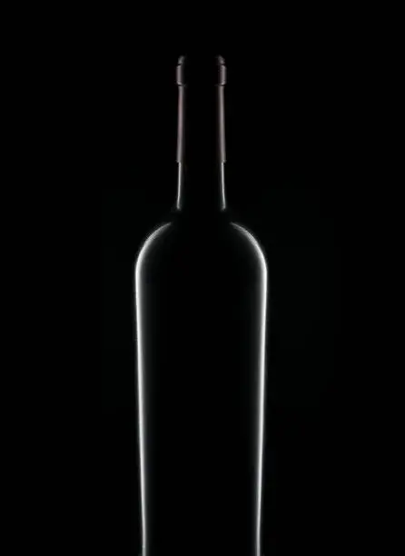 Closeup silhouette of a bottle of red wine over a black background.