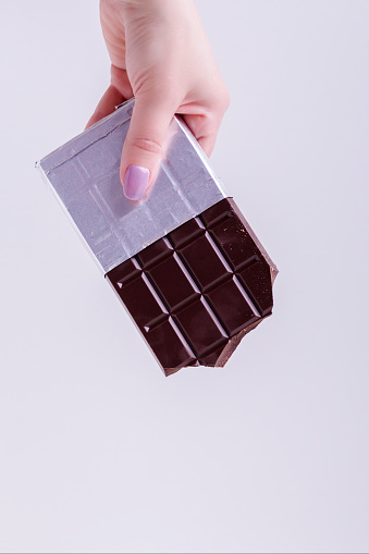 A woman hand holds chocolate bar in foil. Chocolate bar in silver foil.