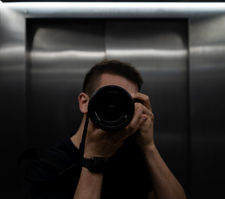 young man photographer making a photo to himself in the mirror in the elevator