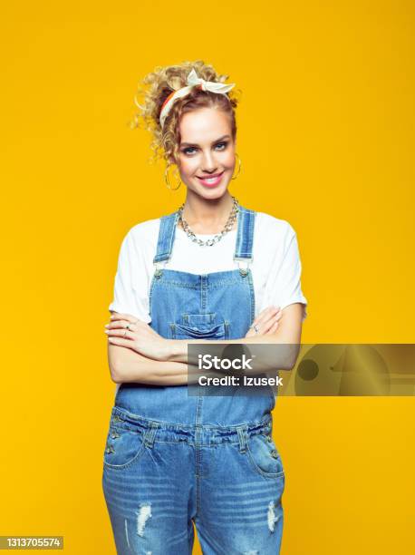Portrait Of Confident Young Woman In Coveralls On Yellow Background Stock Photo - Download Image Now