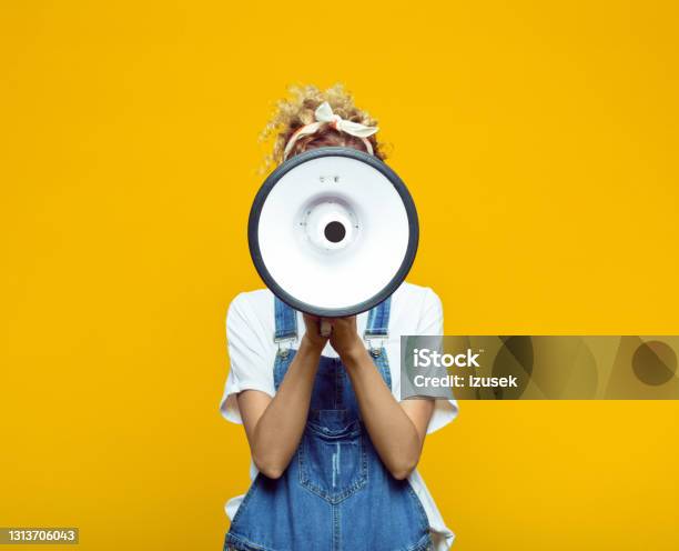 Young Woman In Dungarees Shouting Into Megaphone Stock Photo - Download Image Now - Megaphone, White Color, White People