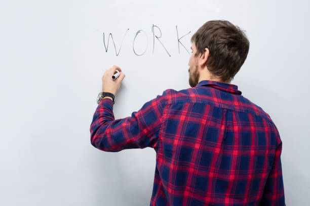 Young man, writing on a white board in the office, makes a presentation. Trainings, education, business. Business and technology concept, view from the back