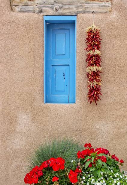 istock Blue window on old adobe structure building with drying chili peppers and flower garden 1313715336