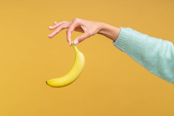 istock Female hand holding a banana with two fingers tips 1313718432