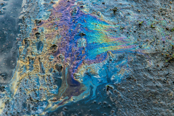 derramamento de produtos petrolíferos. listras oleosas arco-íris em terra e água poluídas - oil slick pouring chemical oil - fotografias e filmes do acervo