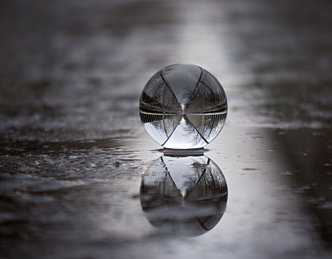Glass ball on the ground in a puddle reflected path with railing
