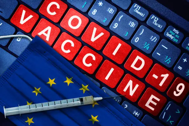 COVID-19 immunization in European Union showing syringe and face mask with EU flag and vaccine message on computer keyboard. Concept of Covid vaccination in the EU.