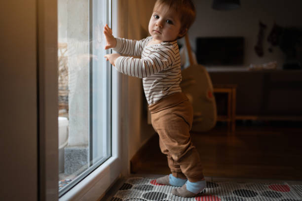istock Baby boy making his first steps while leaning on the glass door and looking at the camera 1313732320