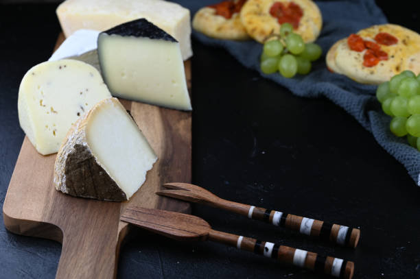 istock Cheese board with snacks and appetizers on a black slate background. Copy space text. Different types of cheeses with grapes, bread pizza and honey. 1313732463