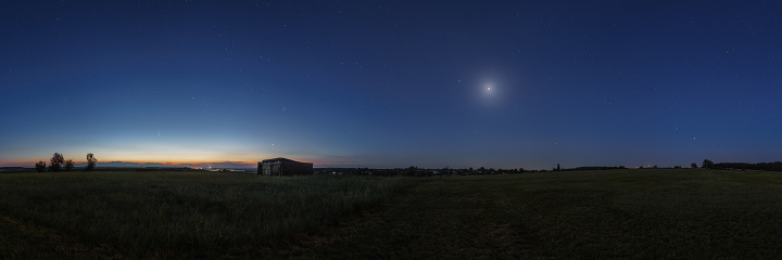 Panorama at dawn of objects in solar system in june 2020 with comet Neowise, Jupiter, Saturn, Mars, Venus and the Moon over field with old barn