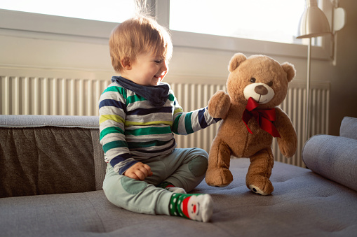 Baby boy playing with white (accented with red fabric with white hearts) large stuffed bear.  The stuffed bear is almost the same size as baby.