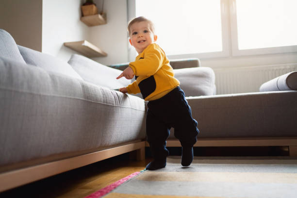 симпатичный мальчик делает свои независимые шаги, опираясь на диван - steps baby standing walking стоковые фото и изобра�жения