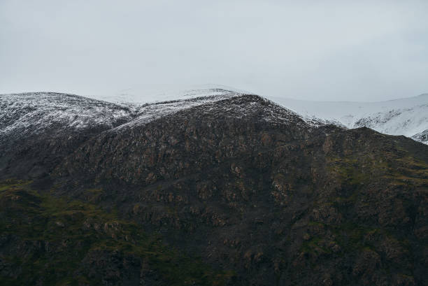 istock Minimalist highlands landscape with snow-capped mountains under cloudy sky. Snowbound high mountain range in overcast weather. Atmospheric minimalism with green mountains, white snow and gray sky. 1313733599