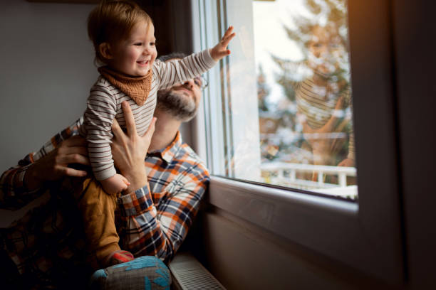 istock Cute baby boy touching window while his father holds him 1313735361