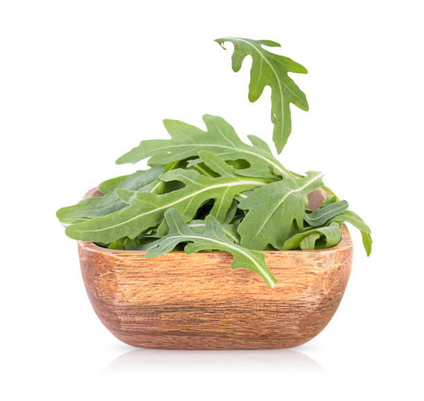 arugula in a wooden bowl arugula in a wooden bowl and one falling leaf. isolated on white background arugula falling stock pictures, royalty-free photos & images