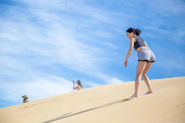 A teenage girls are sandboarding down the sand dune together.