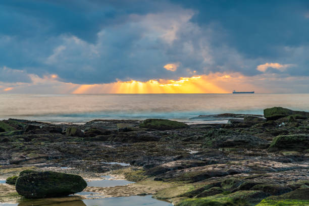 Sunrise seascape with sunrays and ship on the horizon at The Entrance on the Central Coast of NSW, Australia