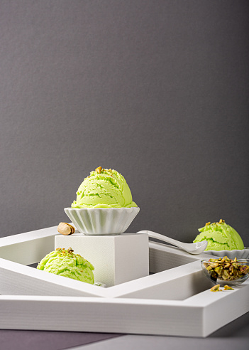 Delicious homemade pistachio ice cream in white bowls with chopped pistachios on gray background. Healthy summer food concept with copy space