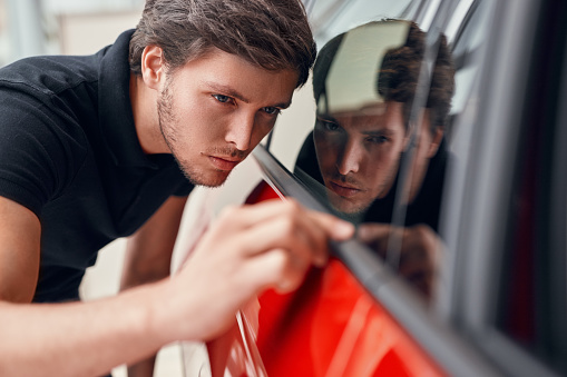 Male customer searching scratches on window of modern vehicle while choosing new car in showroom