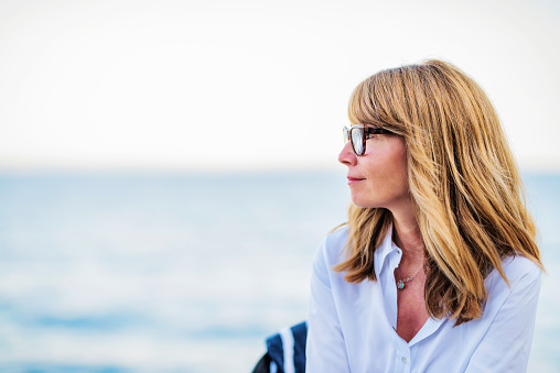 Close-up portrait of happy middle aged woman sitting by the sea.