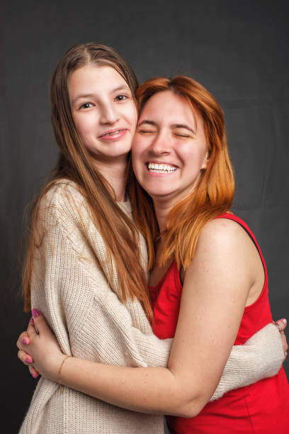 istock Two smiling sisters embraced indoor and looking at camera 1313748499