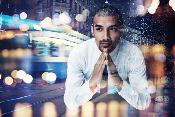 Photo of Shot of a young businessman lost in thought superimposed over a cityscape