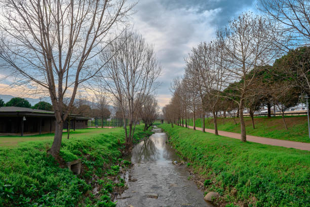 A small river in Bursa that is covered by huge and dried trees together with running and walking path and small building and basketball place.