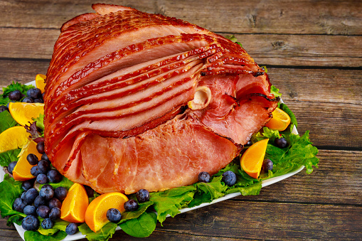 Delicious honey smoked pork ham with fruits on wooden background.