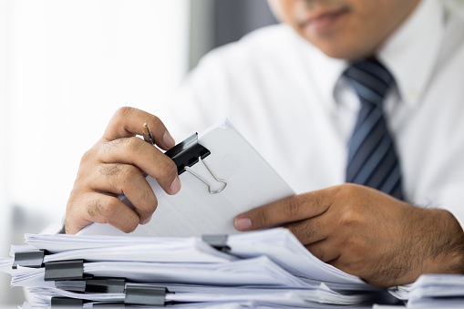 A young business man managing paperwork in the office. Many paperwork that is not finished. Documents in the company about finance and information of the company.