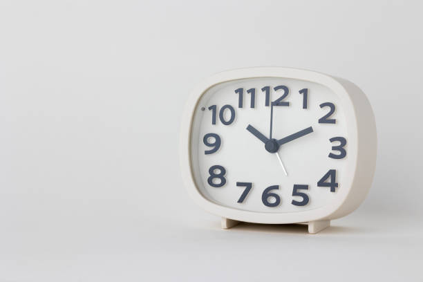 istock Small white alarm clock, black numbers, set the time for 10.10 o'clock, placed on a white table. 1313761267