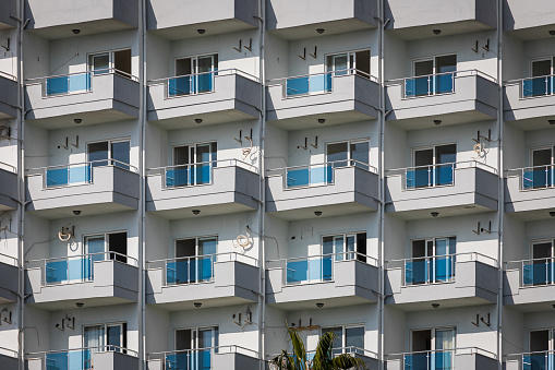A white residential building with flat, identical balconies with ripped air conditioners and broken glass. Balcony pattern