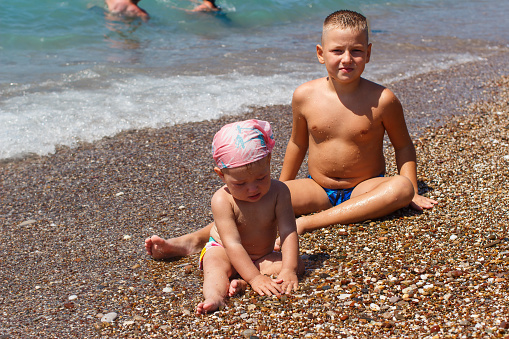 brother and sister play with pebbles on the beach. Tanned children sit on the beach in Turkey