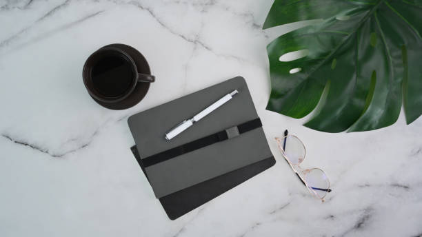 istock Top view of minimal workspace with notebook, eyeglasses and coffee up on marble table. 1313772576