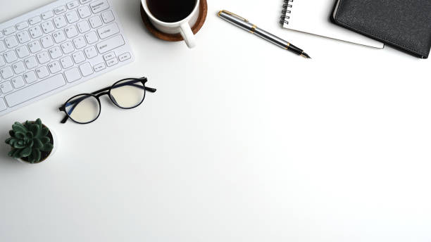 istock Top view of white office desk with notebook, coffee cup, glasses, keyboard and copy space. 1313772645