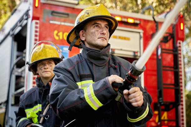 Action Portrait of Male and Female Firefighting Hose Team Low angle view of Caucasian first responders in their 30s holding and supporting nozzle as it shoots straight stream of water. fire hose photos stock pictures, royalty-free photos & images