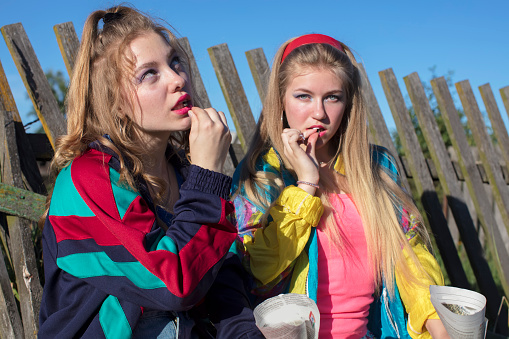 Beautiful country girls dressed in the style of the nineties eating sunflower seeds from a paper bag.