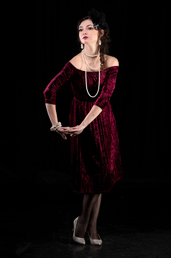A beautiful girl dressed in the style of the 20-30s of the last century posing on a dark background.