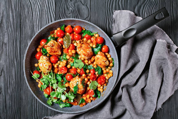 indian cuisine: chickpea and chicken curry of boneless chicken thighs with cherry tomatoes and spinach served with fresh cilantro on a frying pan on a black wooden background, top view, close-up - tomato curry imagens e fotografias de stock