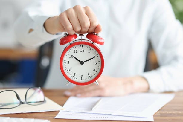 istock Female hand holds red alarm clock at working table 1313782531