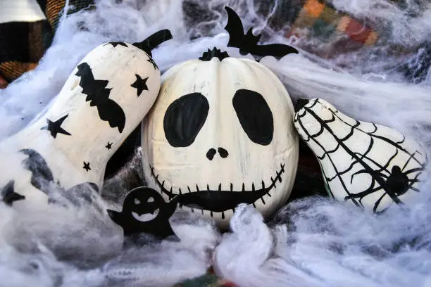 Photo of Halloween background with painted face pumpkins and autumn leaves. Diy. Do it yourself. Halloween decorations, black and white pumpkins, bats, ghosts