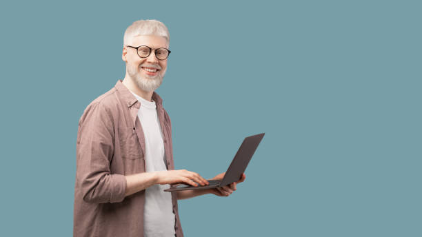 istock Happy albino man using laptop and looking with smile to camera over turquoise background, panorama with copy space 1313785729