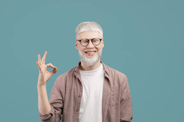 istock Everything is okay. Joyful albino guy doing approval ok gesture with fingers, showing that he is fine, blue studio background 1313786078