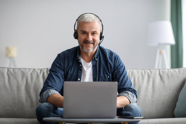 istock Smiling matured man working online, using laptop and headset 1313786128