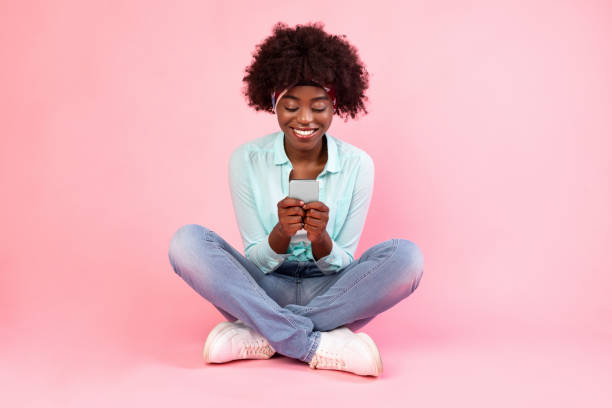 istock Cheerful Black Female Using Smartphone Texting Sitting Over Pink Background 1313787091