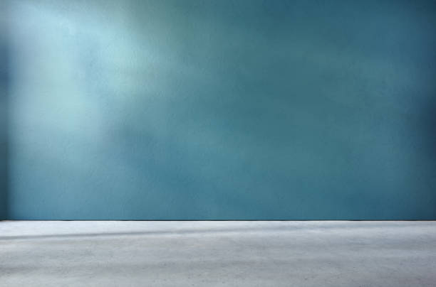 istock Teal textured wall and concrete floor in empty room for displaying your product, light coming through window, industrial atmosphere. 1313787430