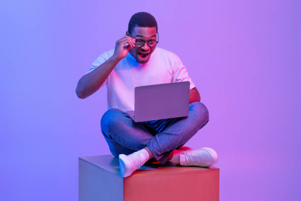 istock Excited Black Male Sitting On Big Cube With Laptop, Looking At Screen 1313787485